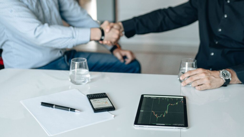 Business meeting with handshake and financial analysis displayed on a tablet.